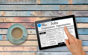 a person looking at recruitment ads on a desk top drinking coffee perm advertising services