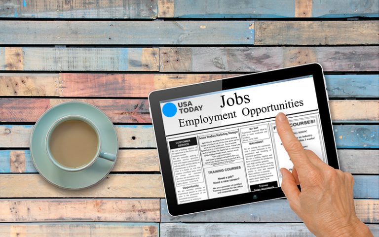 a person looking at recruitment ads on a desk top drinking coffee perm advertising services