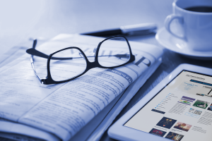 Newspaper and a ipad on a table top with some glasses. place newspaper advertising